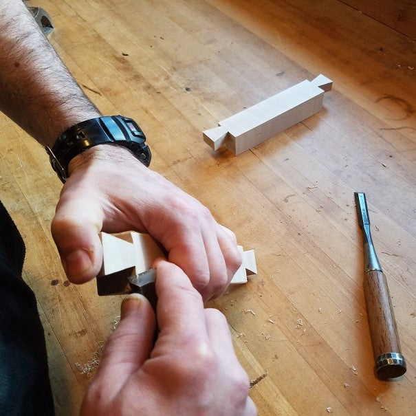 the furniture artist at Mokuzai Furniture uses a chisel to cut dovetails for the feet of a long console table.