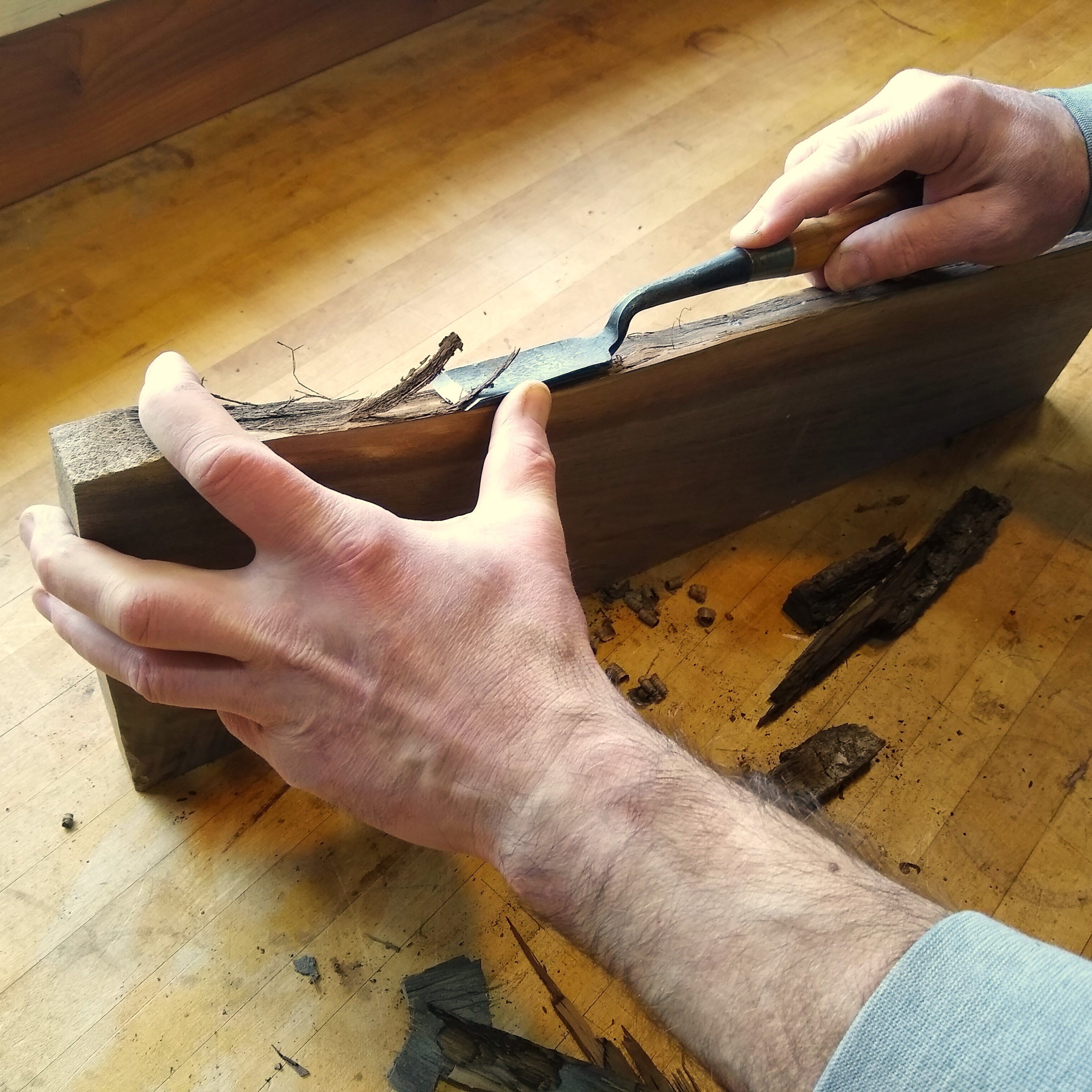 furniture makers at Mokuzai Furniture remove the bark from a live edge table stretcher with a special chisel