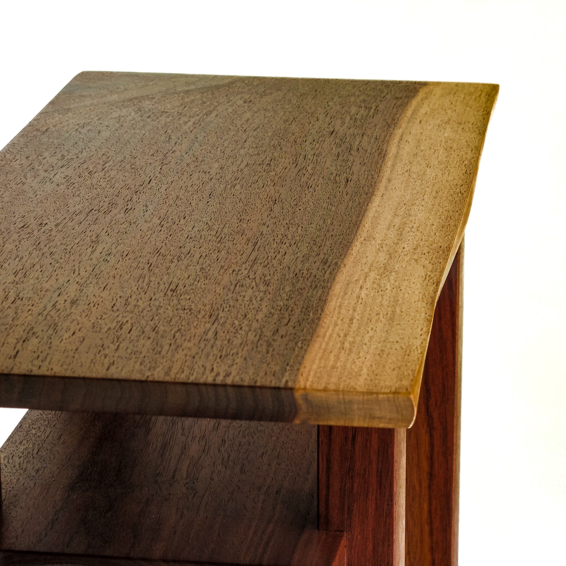 The live edge walnut tabletop of a small end table with two shelves from Mokuzai Furniture.