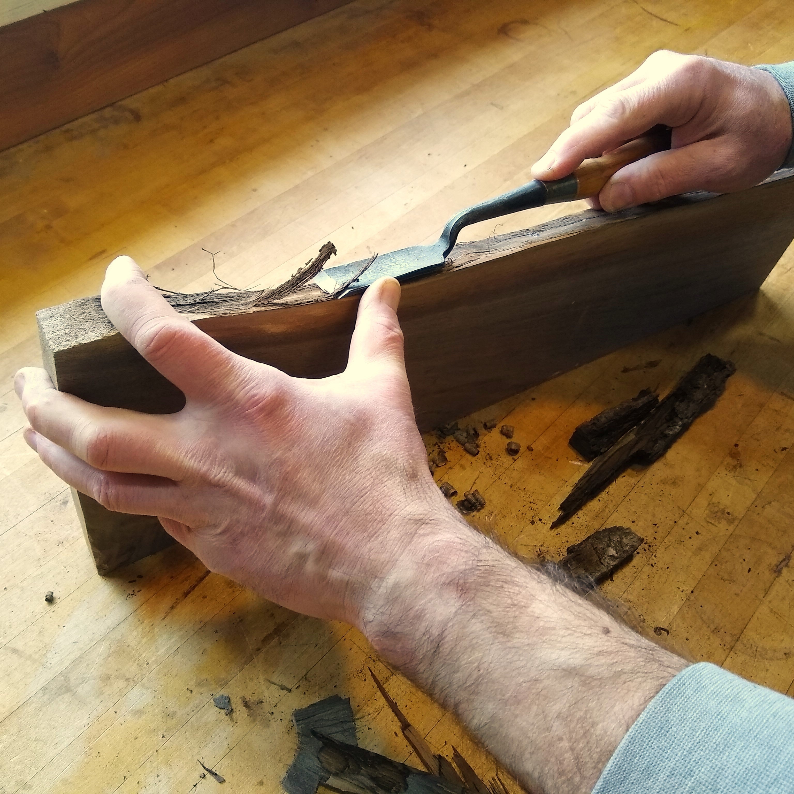 furniture makers at Mokuzai Furniture remove the bark from a live edge table stretcher with a special chisel