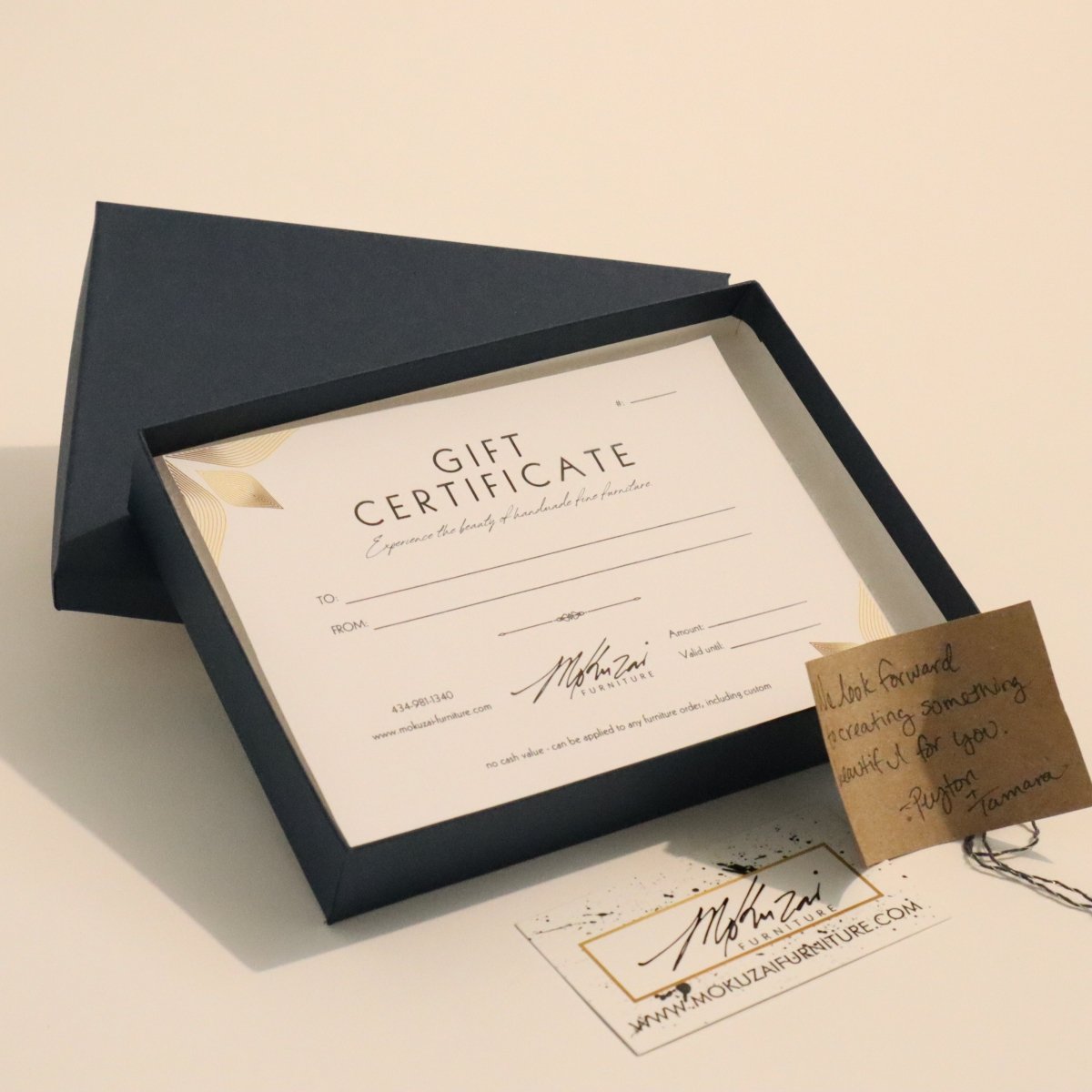 Gift certificate in a navy blue box with a handwritten note from the artists and a business card for luxury wood furniture from Mokuzai Furniture.