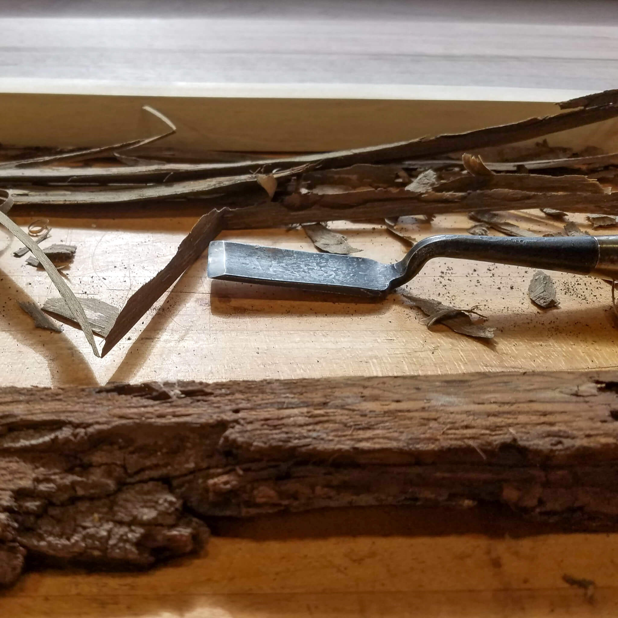 the bark of a live edge table top on a custom end table is removed with a special chisel by the furniture makers at Mokuzai Furniture