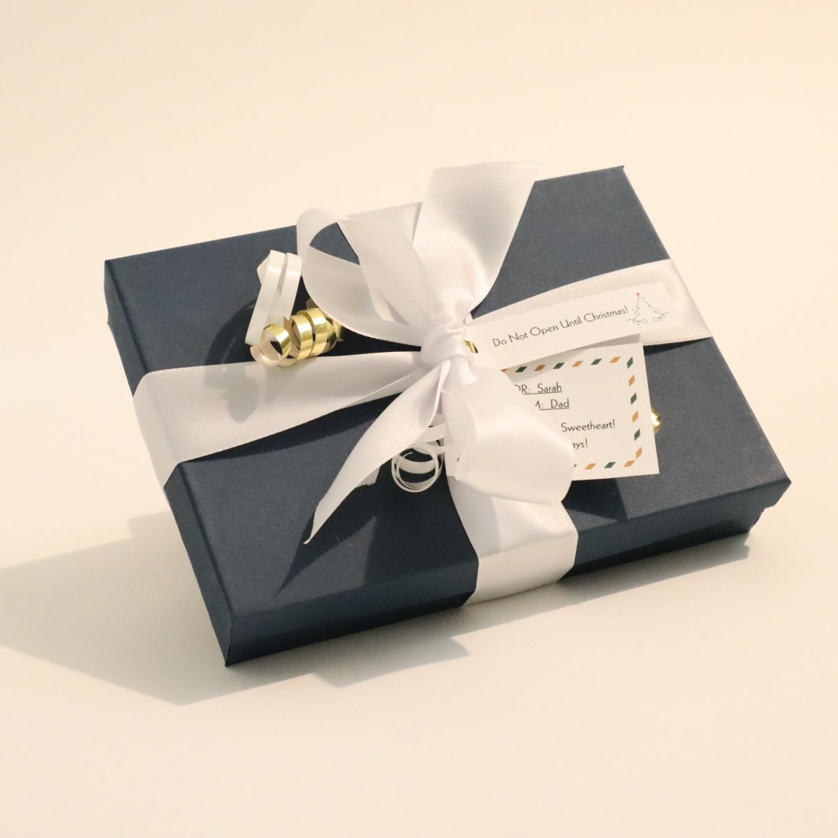 Blue gift box with a white ribbon and card for a luxury christmas gift of custom wood furniture from Mokuzai Furniture.