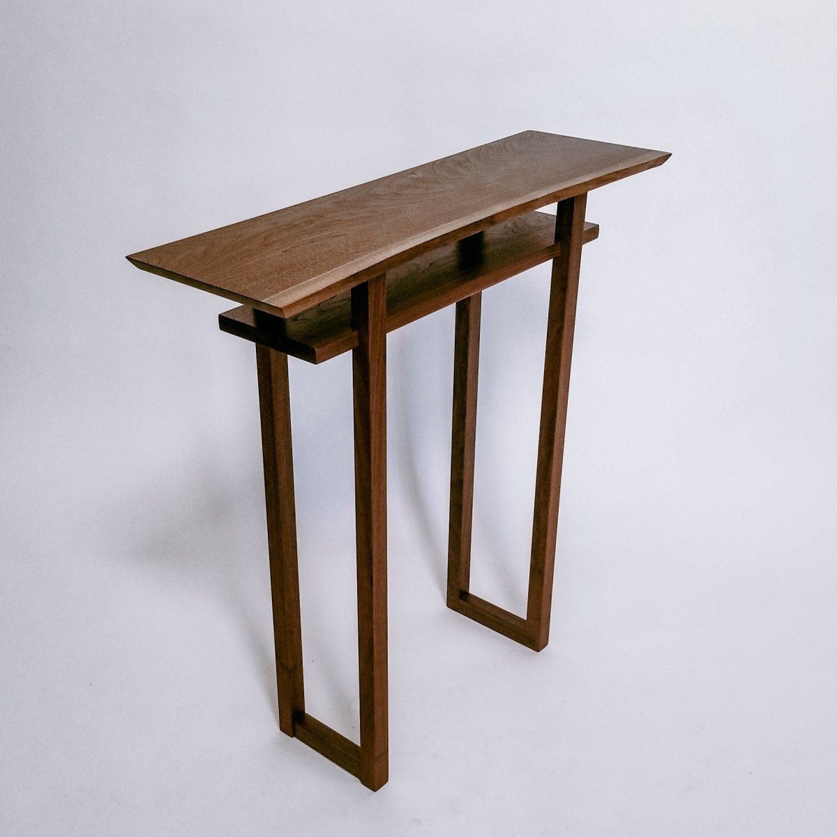 A narrow wooden table created from solid walnut with a live edge table top