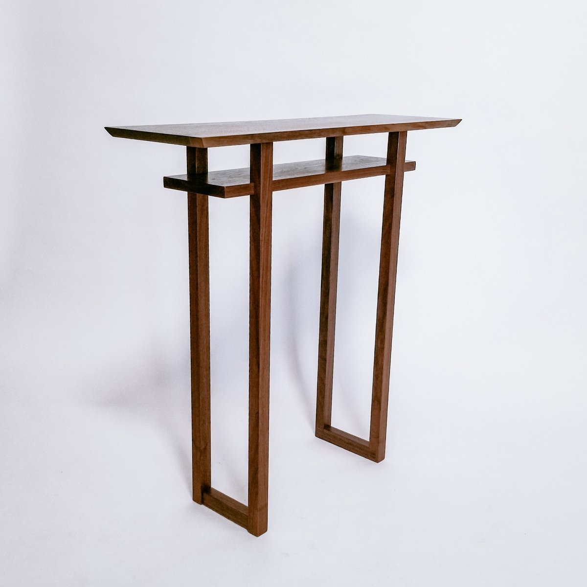 A minimalist console table, handmade from walnut, featuring a live edge table top and inset shelf