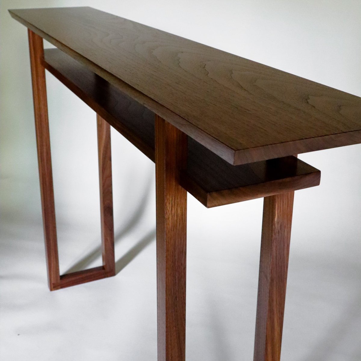 A narrow modern walnut console table with shelf by Mokuzai Furniture.