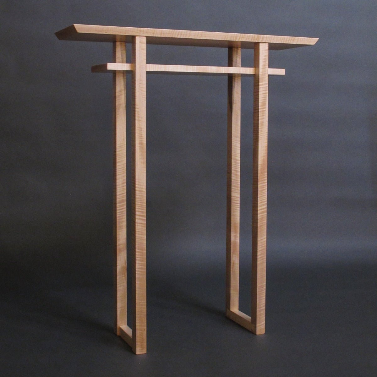 A tall narrow entry table handmade from tiger maple by Mokuzai Furniture.